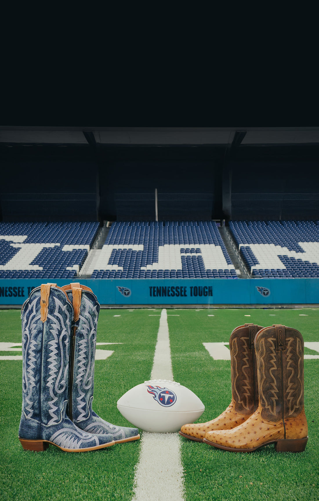 Two pairs of cowboy boots on a football field with a Tennessee Titans logo in the background.