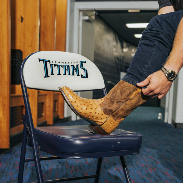 Person wearing cowboy boots on a chair with Tennessee Titans logo in an indoor setting