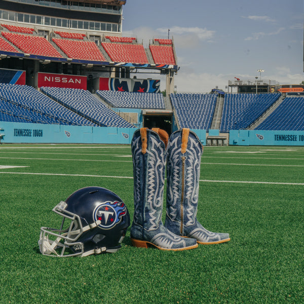 Cowboy boots and a helmet on a football field with stadium seats in the background